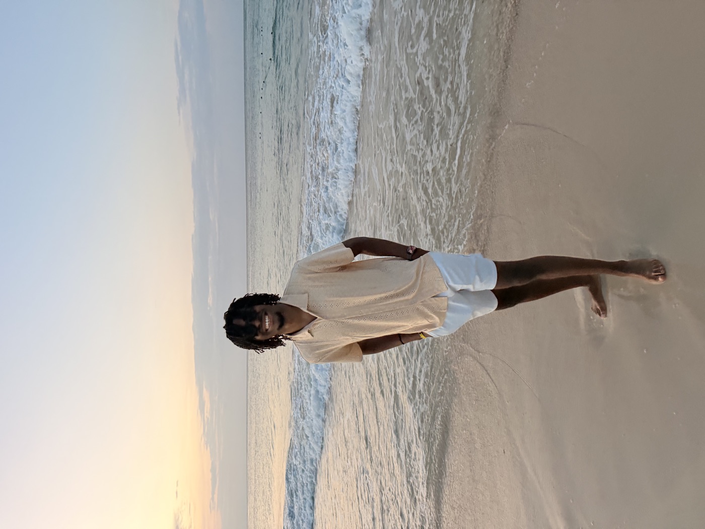 Manuel walking barefoot on a beach at sunset, hands in his pockets, smiling