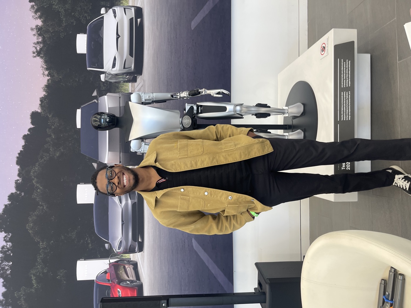Manuel grinning next to Tesla’s Optimus humanoid robot in a showroom